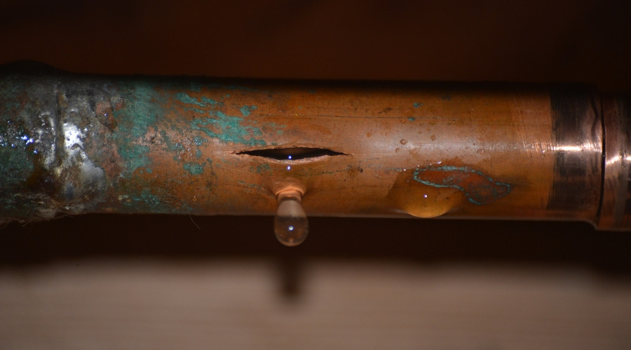 Copper pipe with visible water leak, showing corrosion and droplets forming, relevant to water leak detection and repair services.